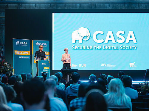 Zwei Maenner auf der Buehne mit Publikum davor