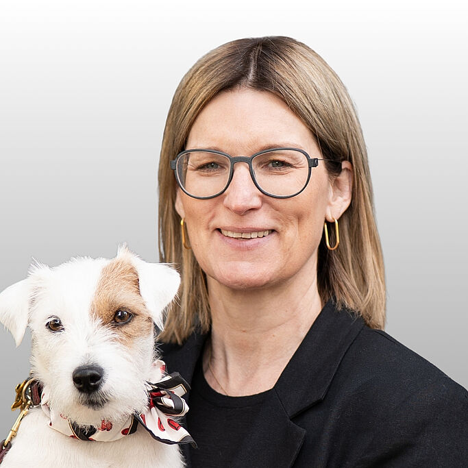 Woman with medium-length blonde hair holding small white dog with brown spots. It is Cornelia Robrahn.