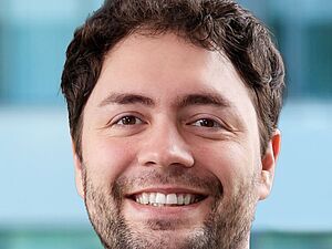 Porträt eines Mannes mit kurzem, lockigem Haar und Bart vor unscharfem Hintergrund. Es handelt sich um Jonas Haferkamp.