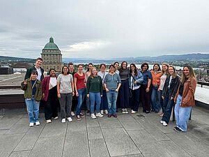 Gruppe von Menschen steht auf einer Dachterrasse mit Blick auf die Stadt Zürich und einen großen Kuppelbau im Hintergrund