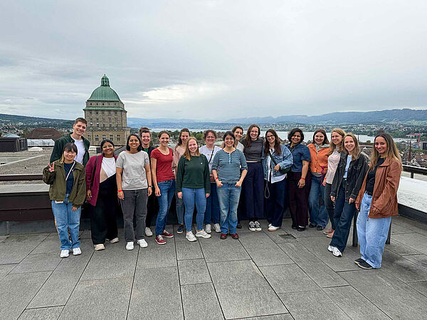 Gruppe von Menschen steht auf einer Dachterrasse mit Blick auf die Stadt Zürich und einen großen Kuppelbau im Hintergrund