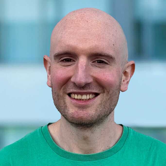 Portrait of a bald man wearing a green t-shirt against a blurred background. It is Julian Loss.
