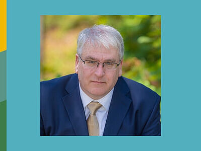 Mann im blauen Anzug vor unscharfem Hintergrund. Es handelt sich dabei um Michael Bailey.