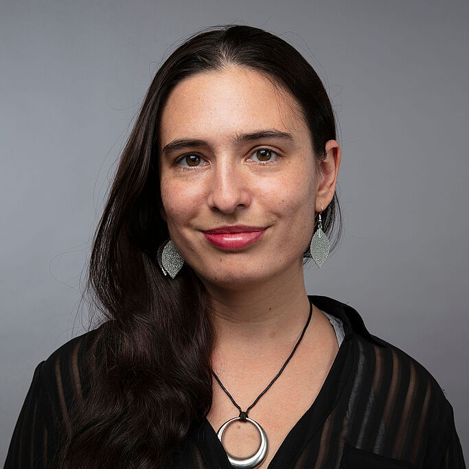 Portrait of a woman with long dark hair wearing a black sweater and a round necklace. It is Sophia Yakoubov.
