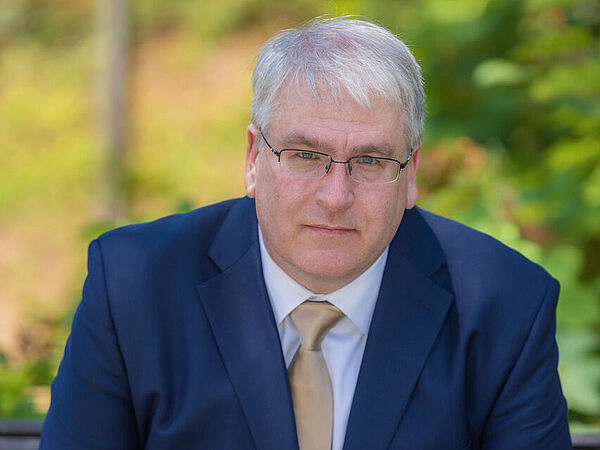 Mann im blauen Anzug vor unscharfem Hintergrund. Es handelt sich dabei um Michael Bailey.