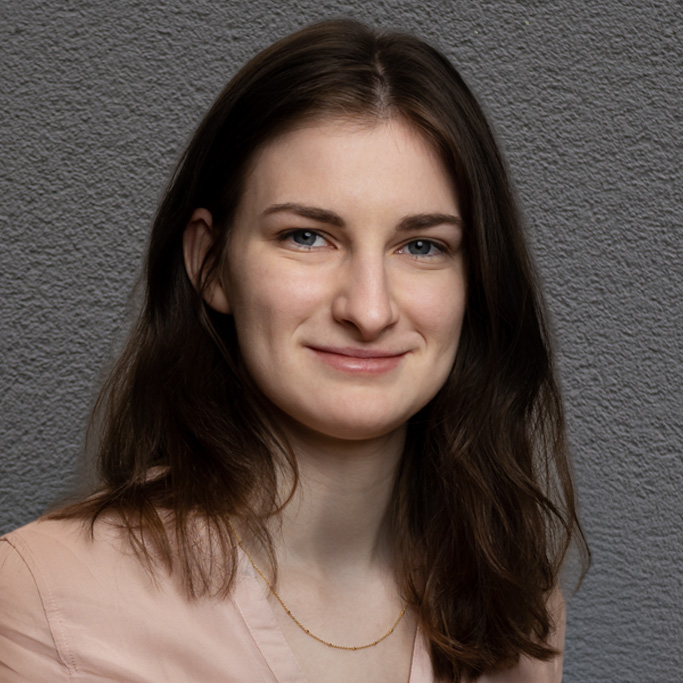 Frau mit schulterlangem, braunem Haar und hellrosa Bluse vor grauem Hintergrund. Es handelt sich um Annika Sengalski.