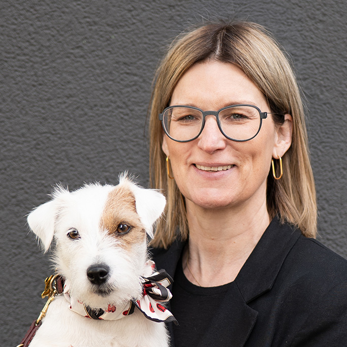 Frau mit mittellangen blonden Haaren hält kleinen Hund mit weißem Fell und braunen Flecken. Es handelt sich um Cornelia Robrahn.