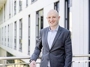 Julian Loss stands in front of a building at Ruhr University Bochum wearing a suit.