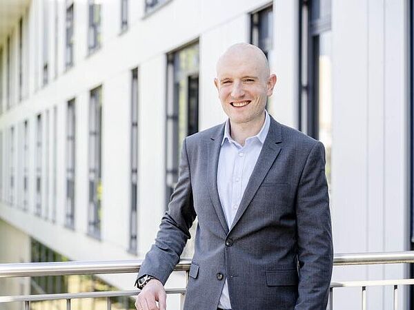 Julian Loss stands in front of a building at Ruhr University Bochum wearing a suit.