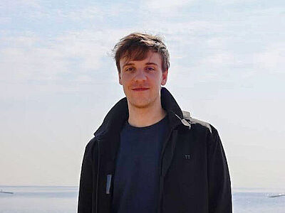 Ein Portrait von CASA PhD Tobias Wienand. Ein Mann mit braunen Haaren steht vor einem hellen Hintergrund.