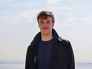 Ein Portrait von CASA PhD Tobias Wienand. Ein Mann mit braunen Haaren steht vor einem hellen Hintergrund.