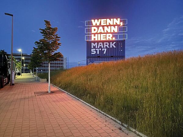Ein Foto der Entwicklungsfläche Mark 51°7 im Dunkeln. Auf einer Leuchttafel steht "Wenn, dann hier."