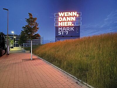 Ein Foto der Entwicklungsfläche Mark 51°7 im Dunkeln. Auf einer Leuchttafel steht "Wenn, dann hier."